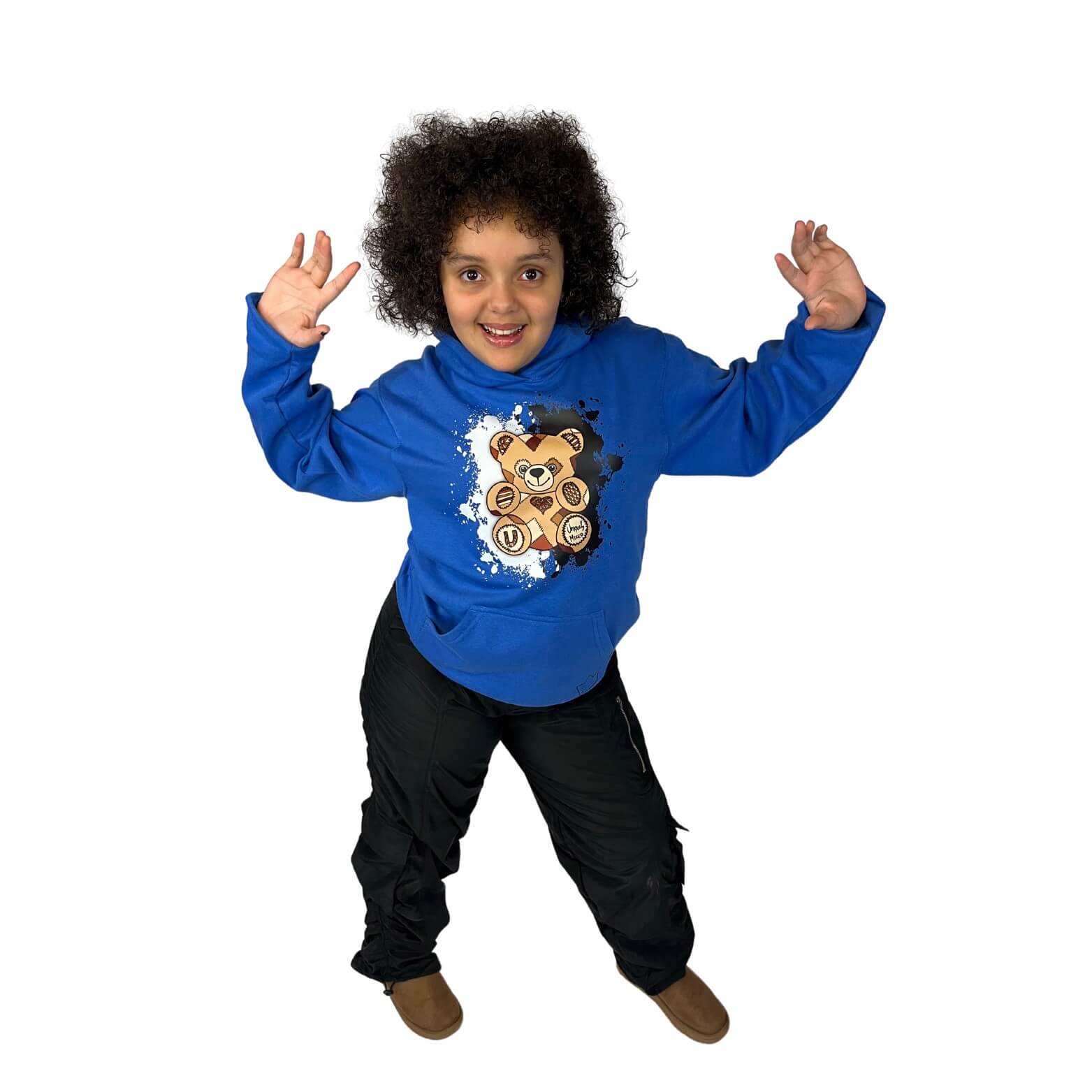 Happy young biracial child wearing a bright blue "I Am Loved" Unity Bear hoodie with a teddy bear graphic, black cargo pants, and brown boots. Playful kids' streetwear celebrating confidence, joy, and positive self-image. 